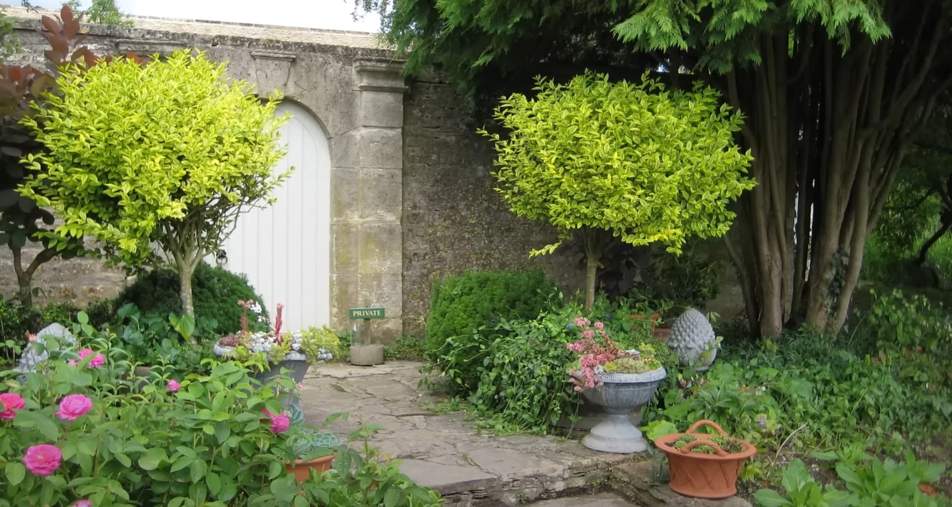 Classic Garden Design with Natural Stone Features and Established Plantings Charming traditional garden with stone archway, potted plants, and mature landscaping