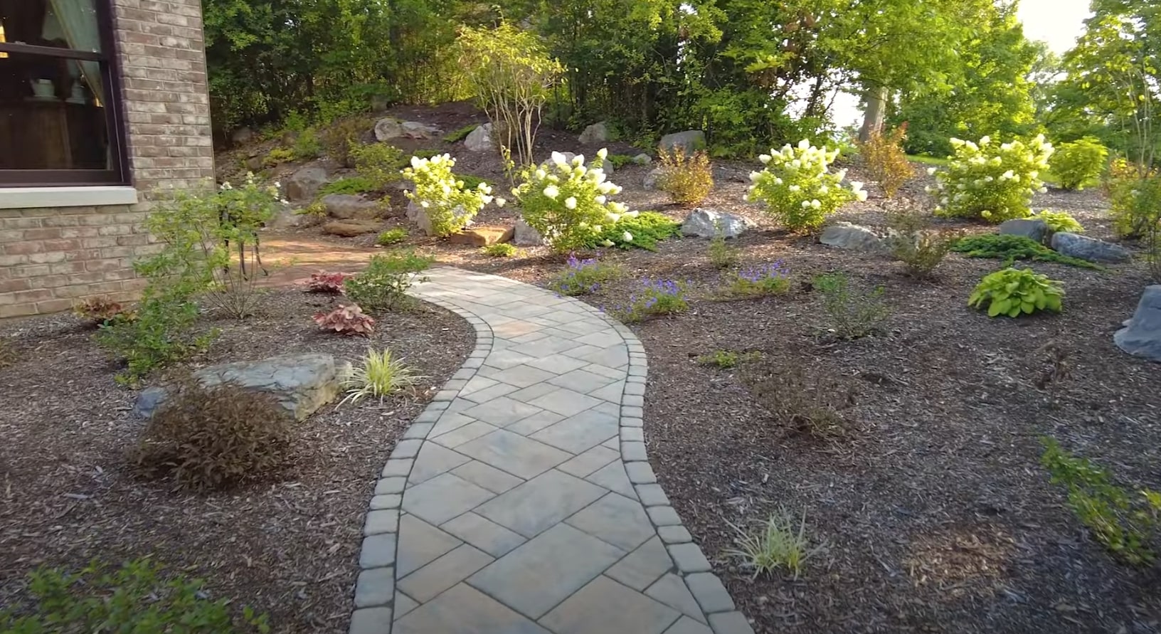Custom Hardscaping - Stone Walkway and Garden Bed Installation Curved stone paver walkway through professionally landscaped garden beds with ornamental plants and lighting